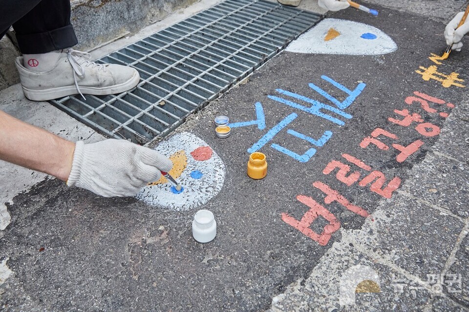 시민들이 빗물받이에서 담배꽁초를 수거하고, 무단투기를 방지하기 위한 아트웍을 그리고 있다. (사진 한국필립모리스)/뉴스펭귄