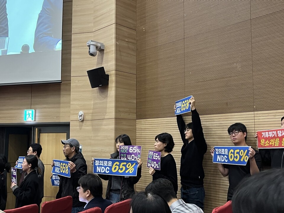정부가 2035년 탄소배출을 2018년 대비 53%~61% 줄이기로 결정했다. 사진은 지난 6일, 시민사회단체 활동가들이 NDC 공청회에서 '65%'를 주장하는 손팻말을 들고 있는 모습. (사진 정도영 기자)